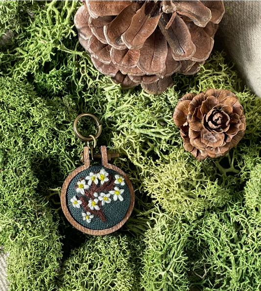 Embroidered stitch marker with floral design on a green moss background