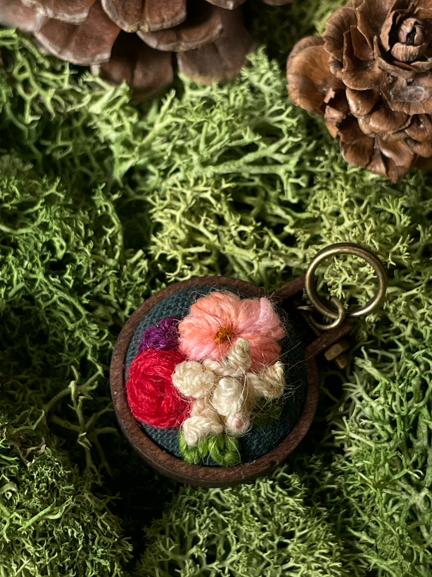 Floral embroidered stitch marker on a green moss background