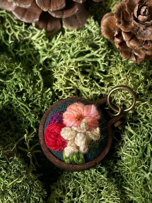 Floral embroidered stitch marker on a green moss background