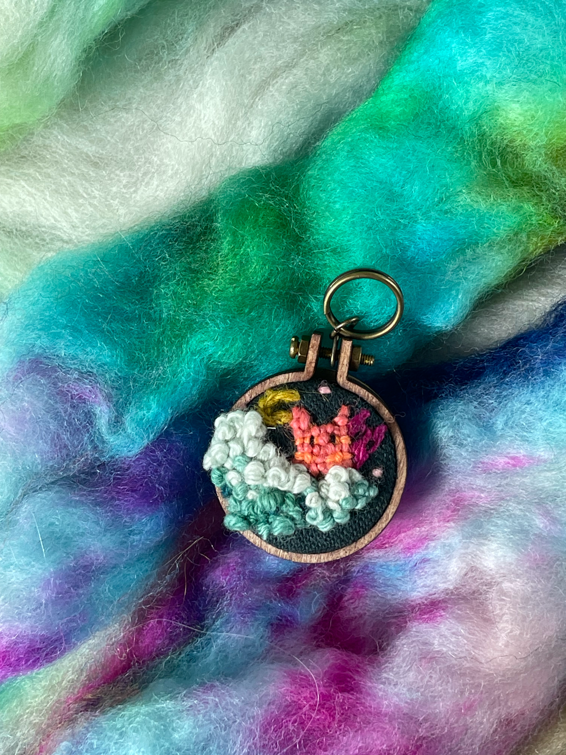 Embroidered stitch marker with clouds, moon and two kitten shaped demons
on a fluffy fleece background