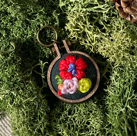 Embroidered stitch marker with floral design on a green moss background
