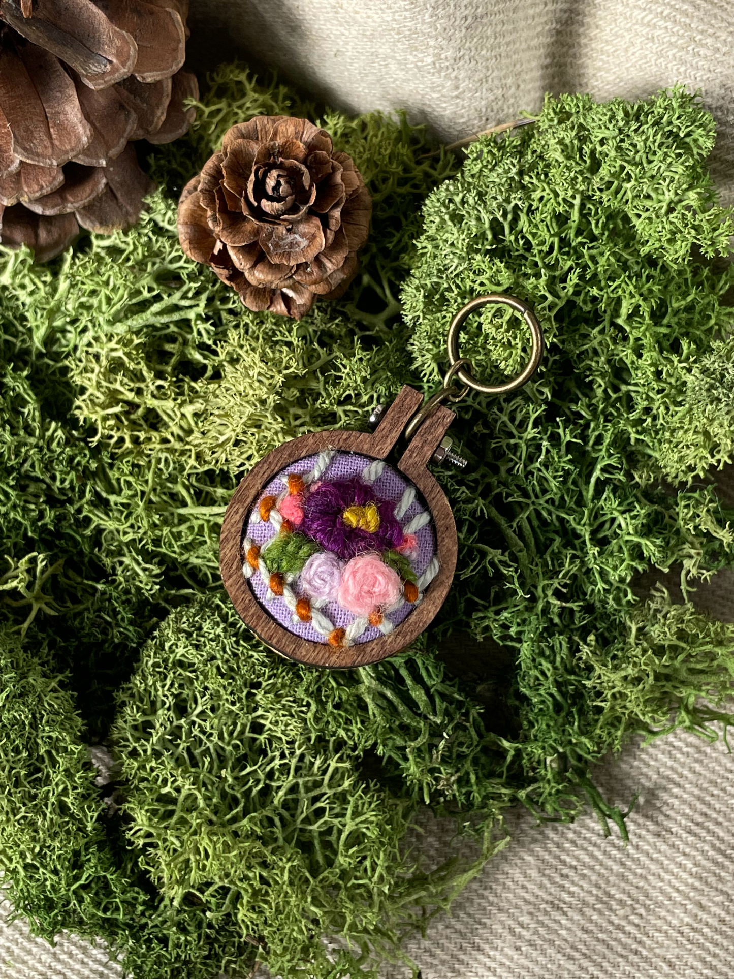 wooden stitch marker embroidered with flowers on a bed of moss