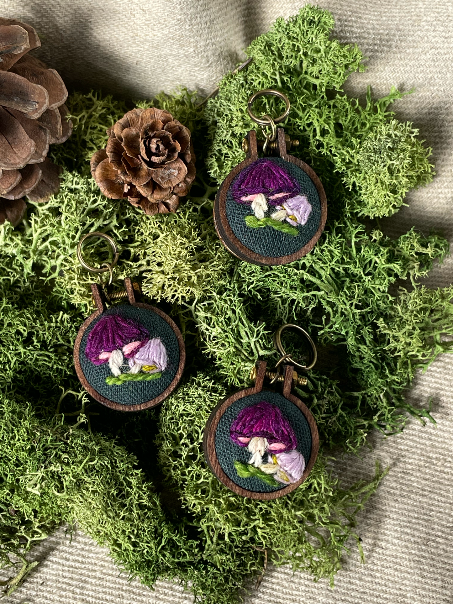Three embroidered stitch markers with purple mushrooms on a green wreath.